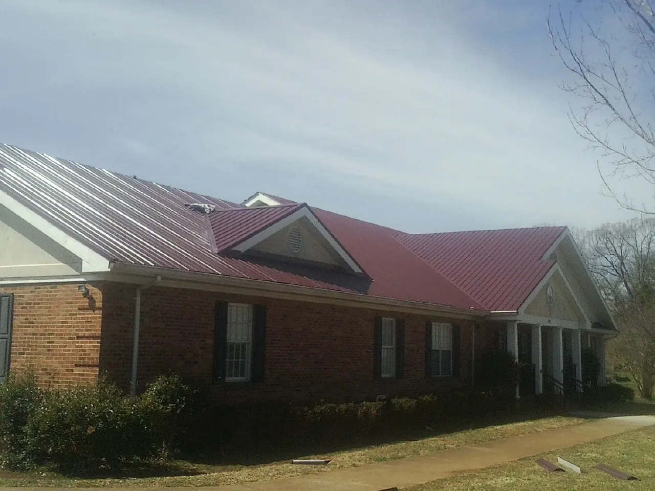 Red metal roof with gabled entries on a long brick building, from a Hail Damage Roof Repair job in Gold Beach