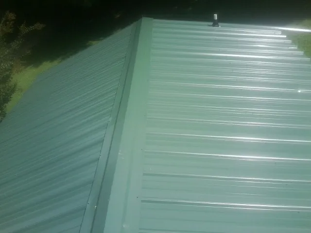 New green metal panels meeting at the ridge of a roof — Flat Roof Repair work by our crew in Gold Beach