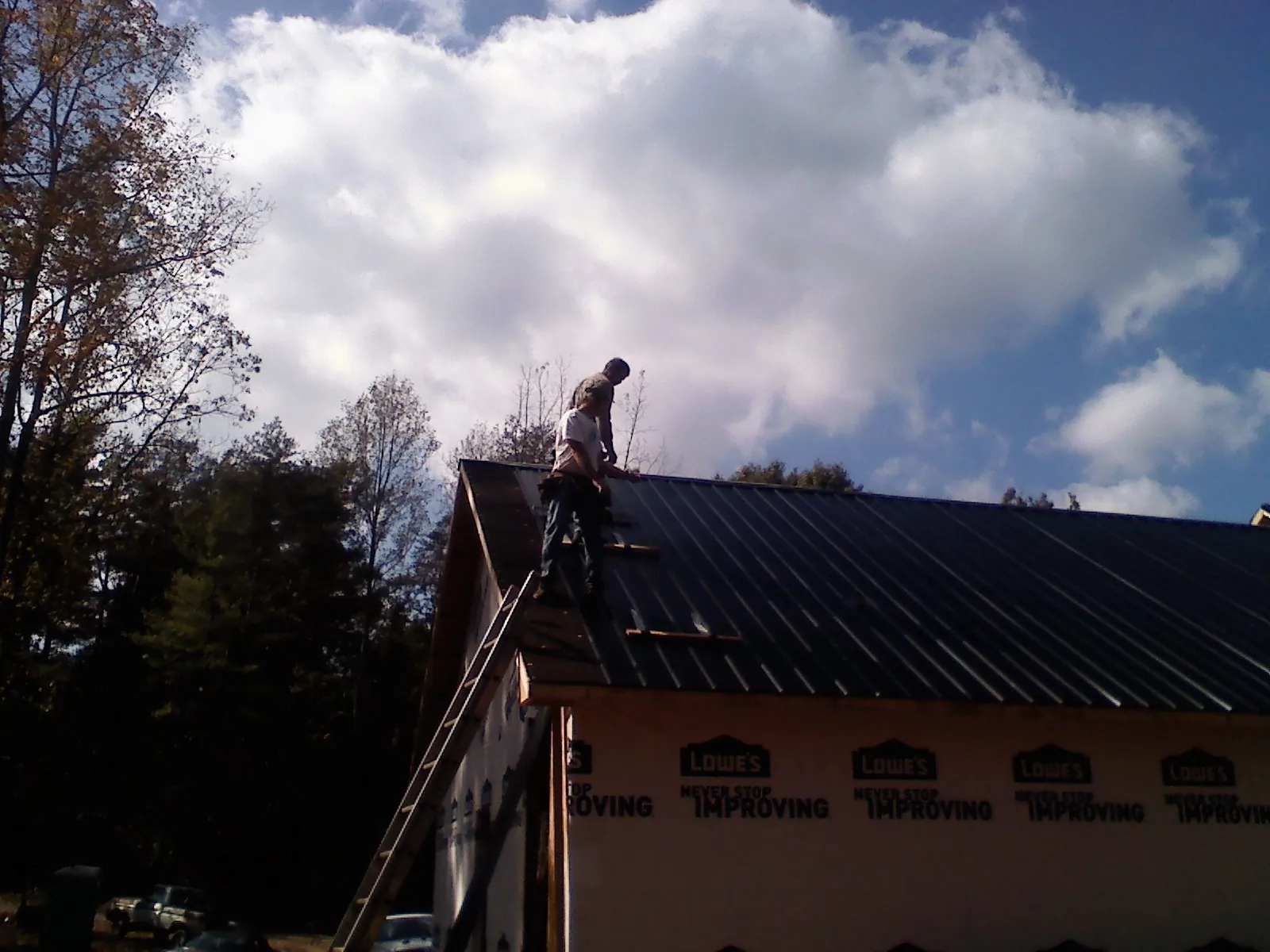 Roofer fastening dark metal panels high against a cloudy sky, from a Roof Inspection job in Gold Beach