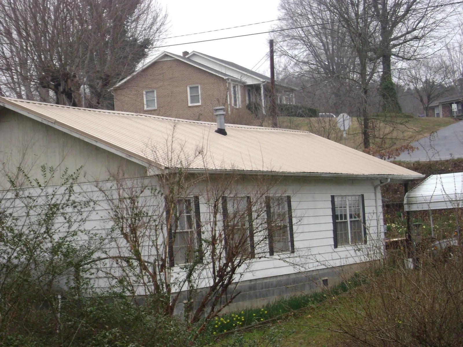 Tan metal roof on a white sided house set into a hillside — Commercial Roofing by Roofing Brothers in Gold Beach