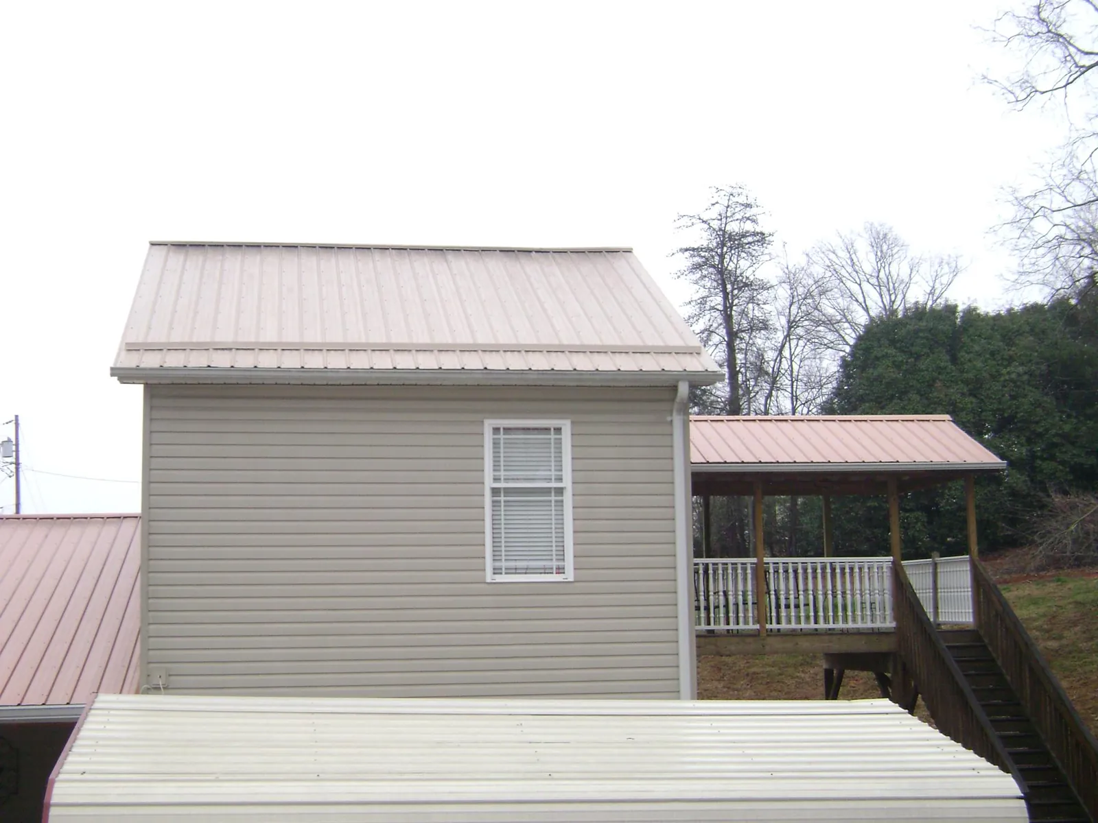 Tan metal roofs on a two story addition and attached porch, from a Roof Replacement job in Gold Beach